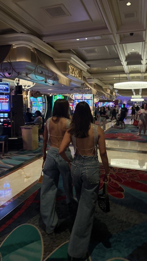 Two friends in backless sequin tops and wide-leg jeans walking through a casino
